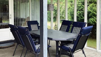 Un patio techado con mesa y sillas, un ventanal de vidrio y vistas al verdor.