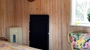 Ein Zimmer mit einem Bett, einem weißen Schrank, einer schwarzen Tür und einem Korbstuhl mit einem blumigen Kissen.