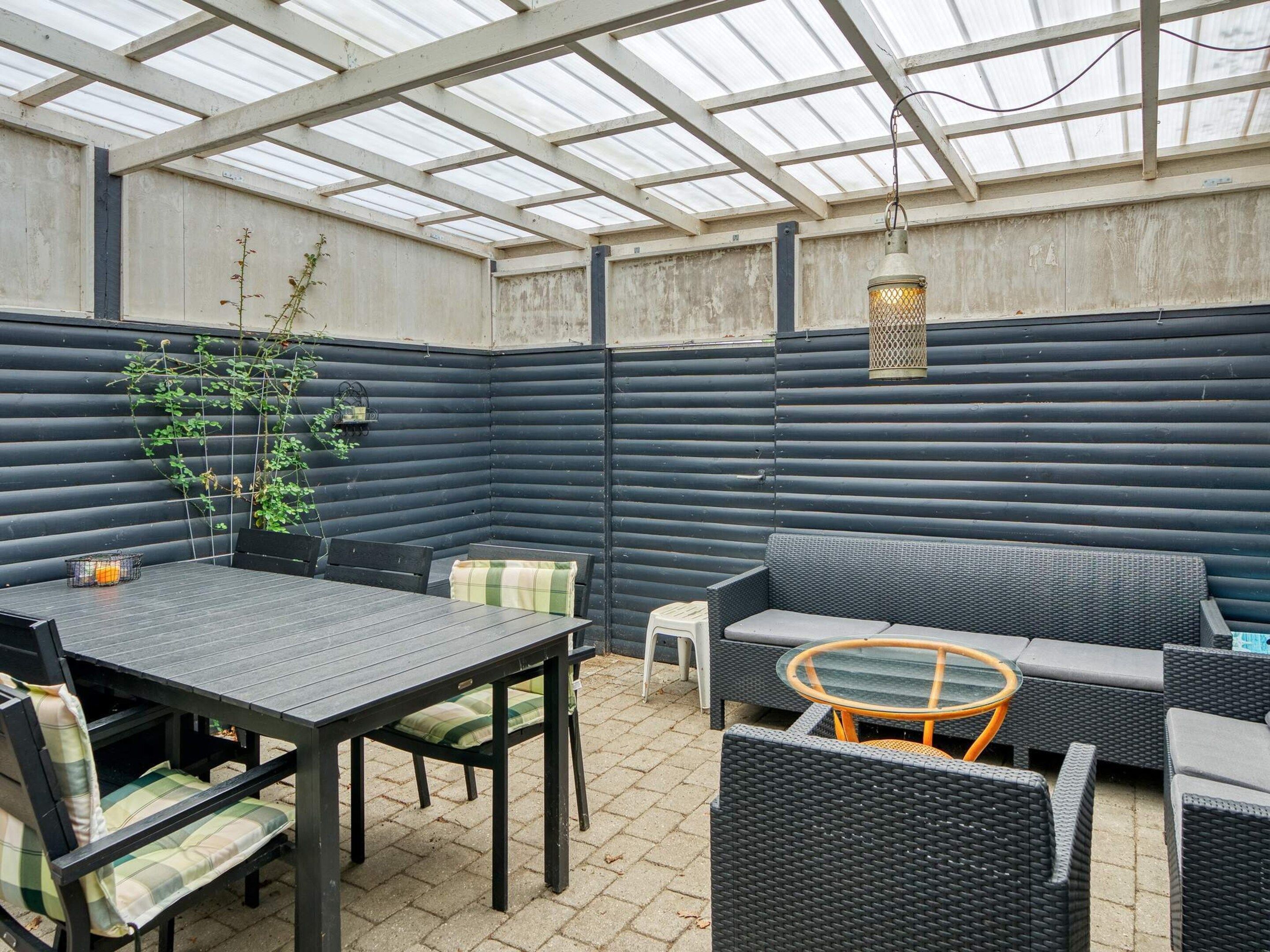 A covered patio area with a table and chairs, a sofa, and a small round table with a glass top.