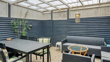 A covered patio area with a table and chairs, a sofa, and a small round table with a glass top.