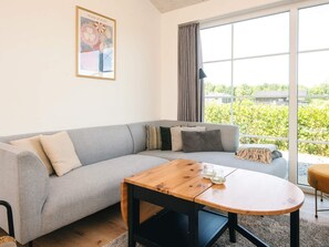 A modern living room with a grey sofa, a round wooden coffee table, and a large window with curtains. - 5 Star Holiday Home in Ansager (Ansager)