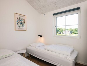 A room with a single bed, a small bedside table, a framed botanical print on the wall, and a window with a view of greenery and buildings. - 5 Star Holiday Home in Ansager (Ansager)