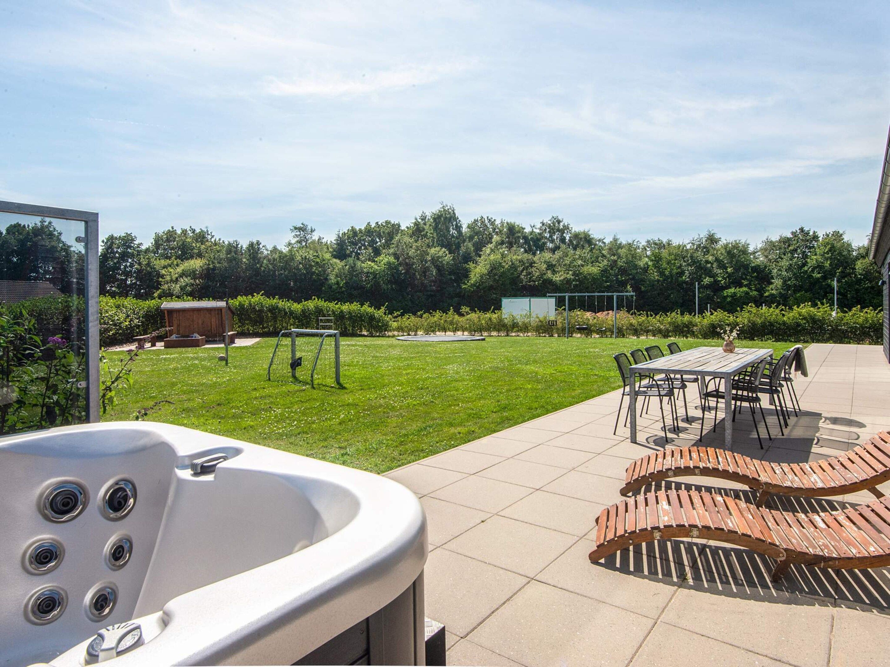Un espace patio doté d’un jacuzzi, de sièges d’extérieur et offrant une vue sur une pelouse verdoyante et des arbres.