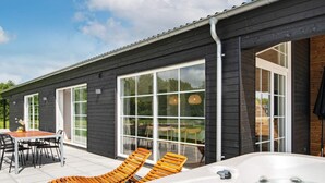 A modern building with large windows, a patio with lounge chairs, and a hot tub. - 5 Star Holiday Home in Ansager (Ansager)