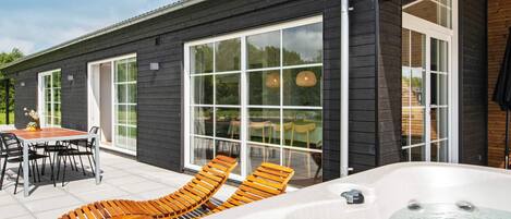 A modern building with large windows, a patio with lounge chairs, and a hot tub.