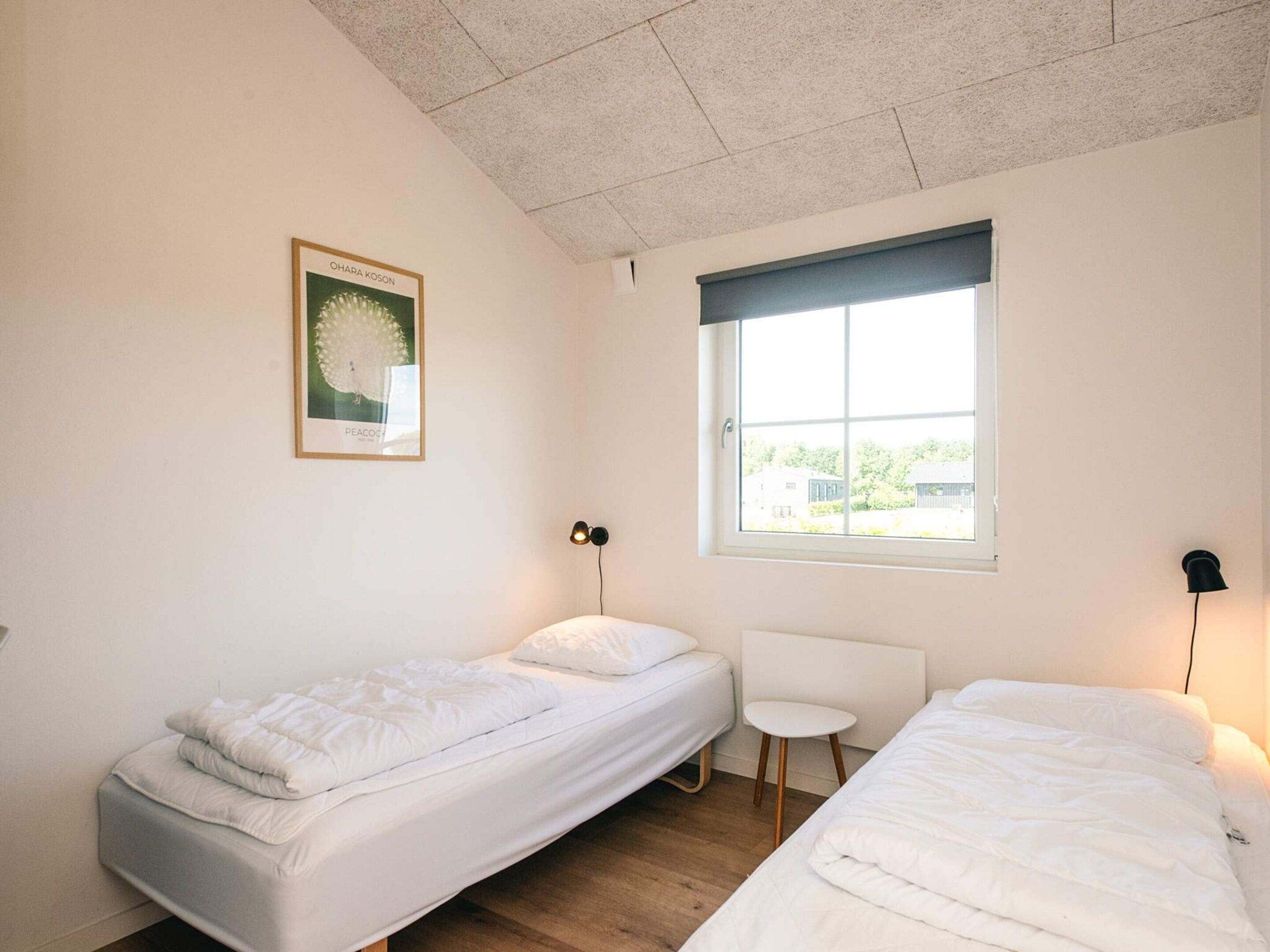 A bedroom with two single beds, a small white chair, a window with a view, and a framed picture on the wall.