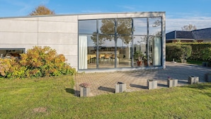 A modern building with large glass windows, a paved courtyard, and a well-maintained lawn. - 6 Person Holiday Home in Vaeggerlose (Vaeggerlose)