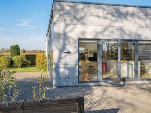A modern building with a glass entrance, a paved outdoor area, and a garden with various plants. - 6 Person Holiday Home in Vaeggerlose (Vaeggerlose)