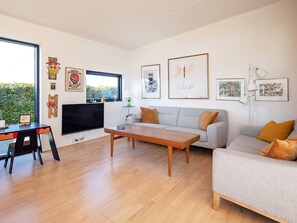 A modern living room with a sofa, coffee table, and a TV. There are framed artworks on the walls and a window with a view. - 6 Person Holiday Home in Vaeggerlose (Vaeggerlose)