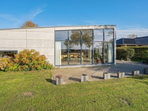 A modern building with large glass windows, a paved courtyard, and a well-maintained lawn. - 6 Person Holiday Home in Vaeggerlose (Vaeggerlose)