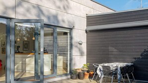 A modern building with a glass door entrance, a patio area with a table and chairs, and potted plants. - 6 Person Holiday Home in Vaeggerlose (Vaeggerlose)