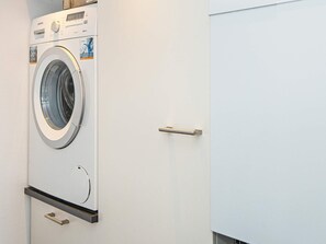 A front view of a washing machine in a laundry room with a door and a handle. - 8 Person Holiday Home in Ebeltoft (Ebeltoft)