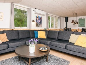 A modern living room with a grey sectional sofa, a round coffee table, and a small white vase with purple flowers. - 8 Person Holiday Home in Ebeltoft (Ebeltoft)