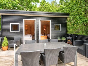 A log cabin with two bedrooms, a deck with wicker furniture, and a wood-burning stove. - 8 Person Holiday Home in Ebeltoft (Ebeltoft)