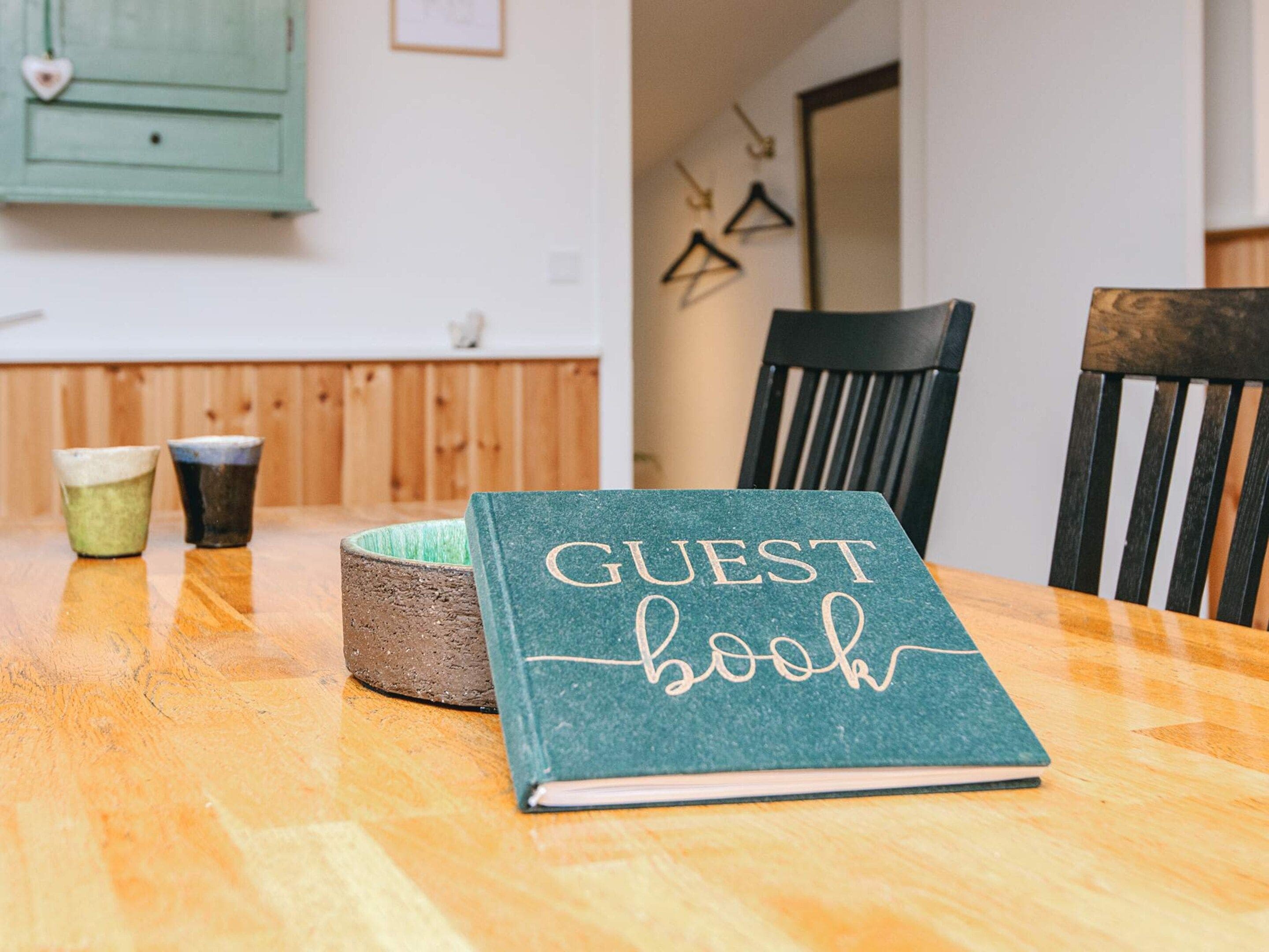 A wooden table with a green guest book, two ceramic cups, and a rustic bowl.