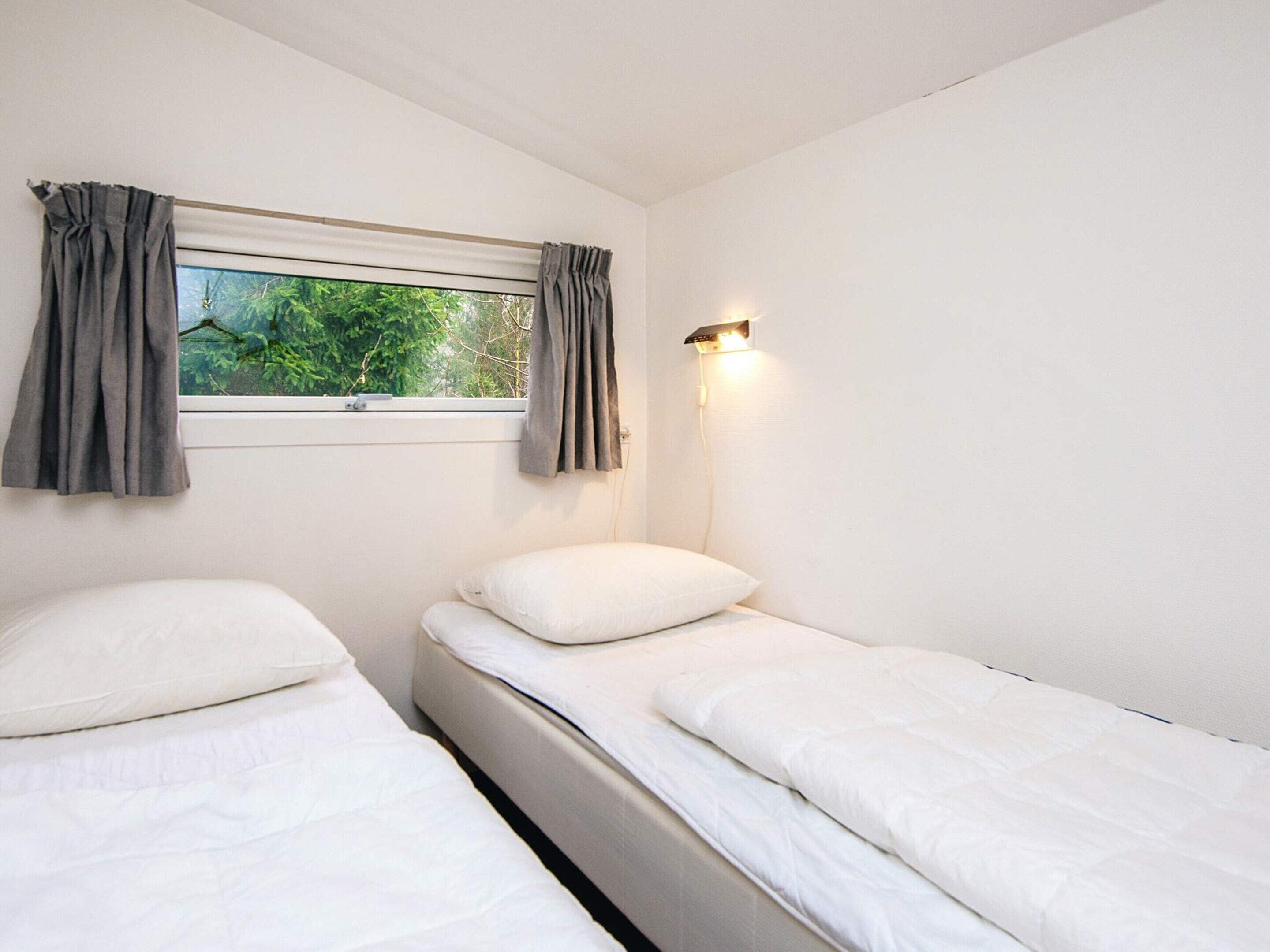 A room with two single beds, a window with curtains, and a wall-mounted light fixture.