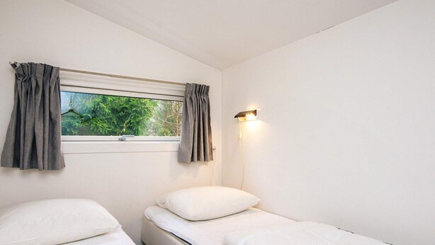 A room with two single beds, a window with curtains, and a wall-mounted light fixture.