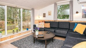 A modern living room with a sofa, a coffee table, and a large window offering a view of a garden.