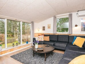 A modern living room with a sofa, a coffee table, and a large window offering a view of a garden. - 8 Person Holiday Home in Ebeltoft (Ebeltoft)