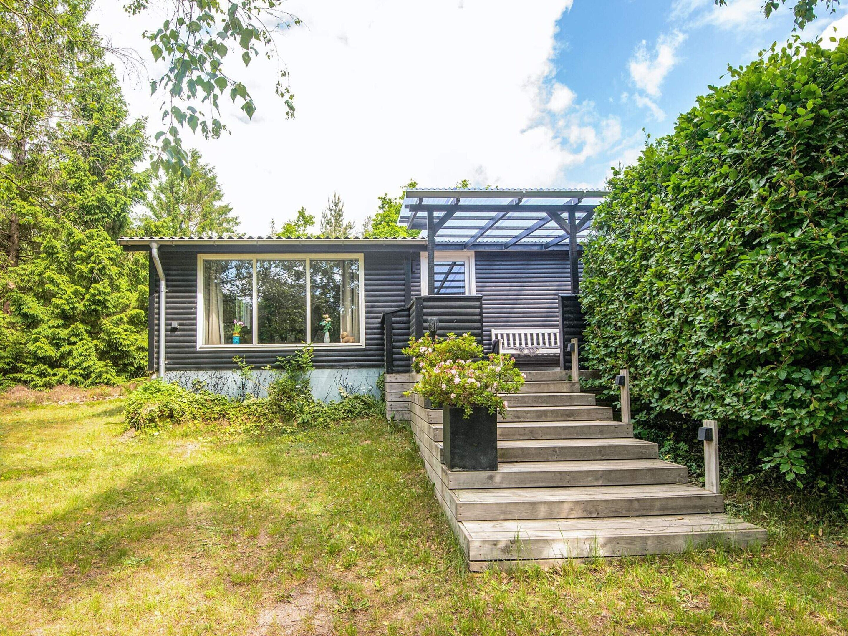 En stuga med en veranda, några trappsteg och ett fönster med utsikt över en trädgård.