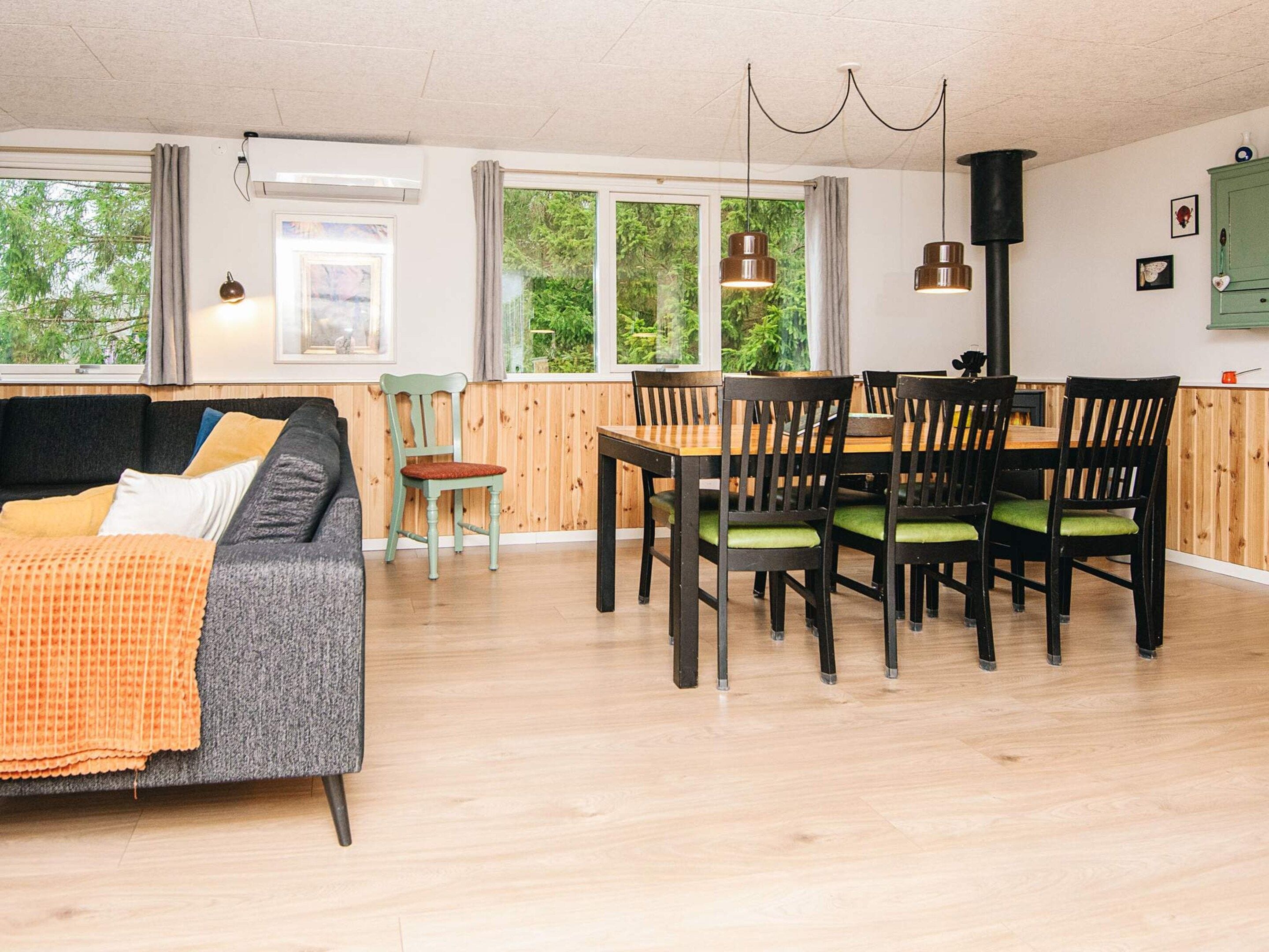 A modern living room with a sofa, a dining table with chairs, and a kitchen area with a stove.