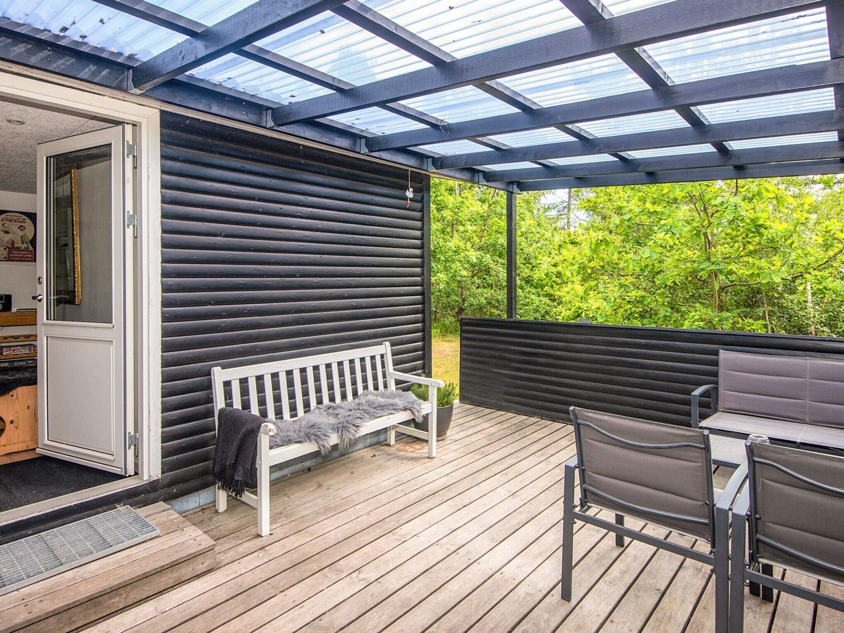 Una terraza de madera con zona cubierta, un banco blanco y una mesa con sillas.