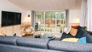 A modern living room with a large window, a flat-screen TV, a fluffy dog, and a cozy sofa.