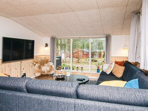 A modern living room with a large window, a flat-screen TV, a fluffy dog, and a cozy sofa. - 8 Person Holiday Home in Ebeltoft (Ebeltoft)