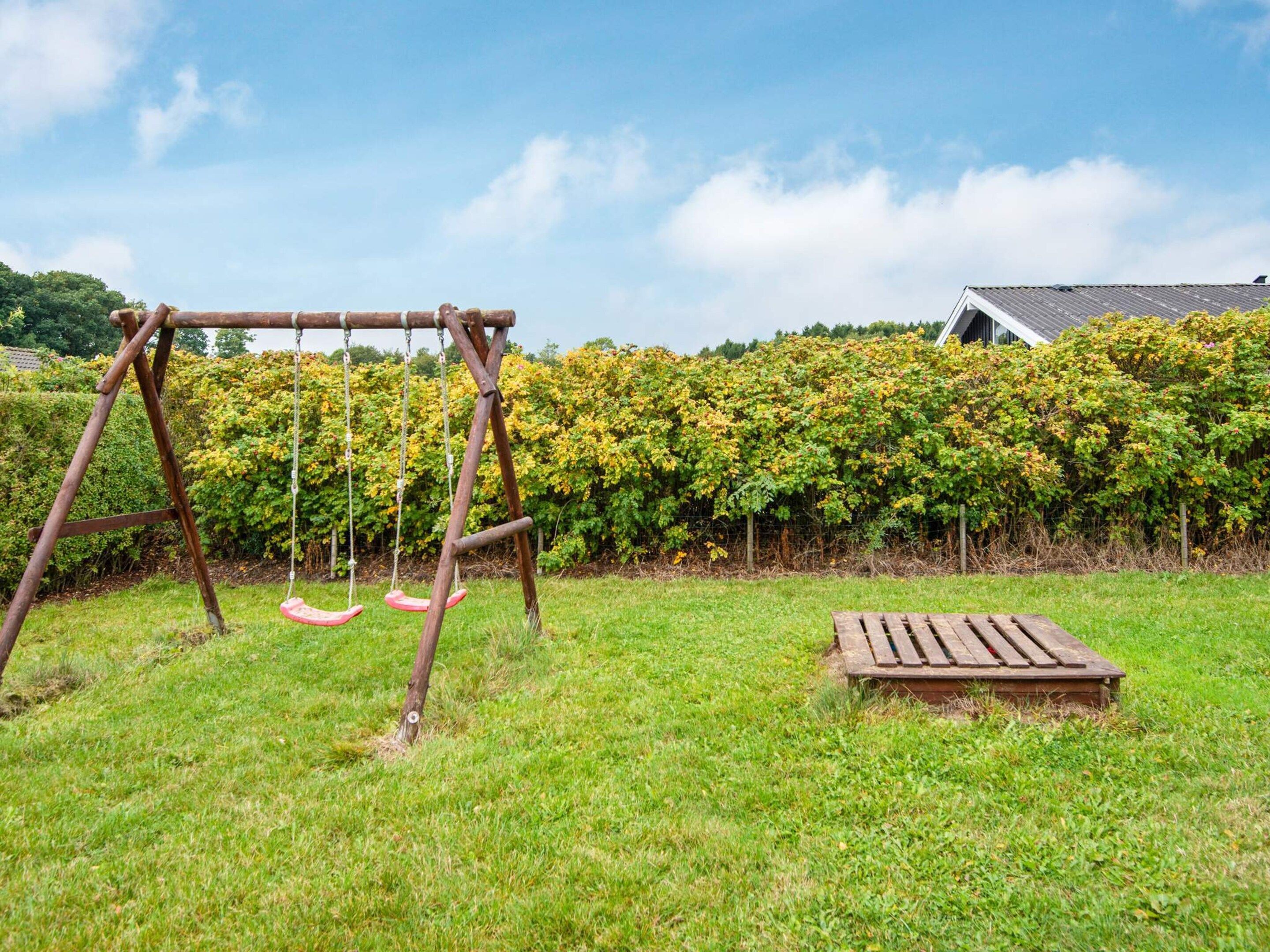 A wooden swing set in a grassy yard with a hedge and a house in the background.
