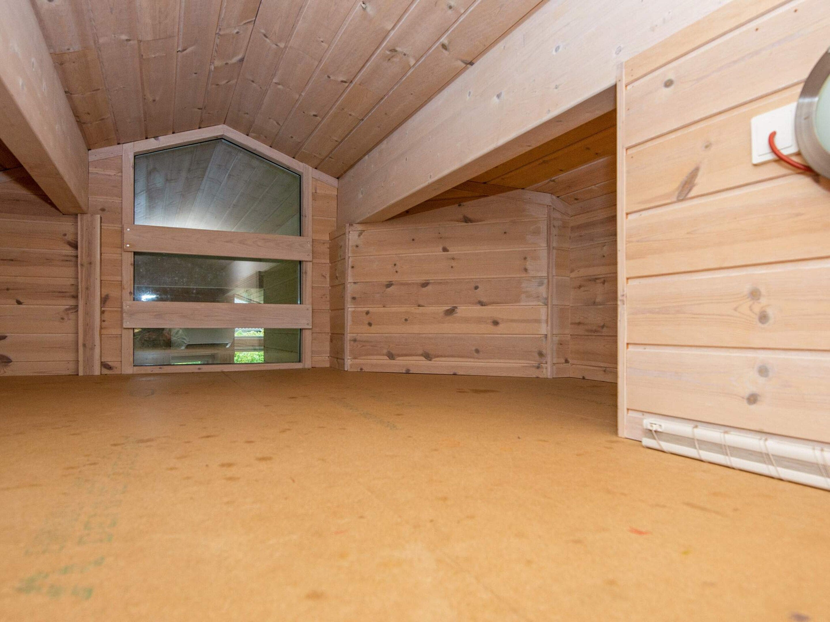 A room with a sloped ceiling, wooden walls, and a large window.