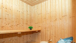 A wooden sauna room with a bench, a small shelf with a plant, a wooden bucket, and a red container. - 4 Star Holiday Home in Juelsminde (Horsens)