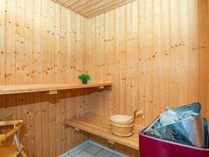 A wooden sauna room with a bench, a small shelf with a plant, a wooden bucket, and a red container. - 4 Star Holiday Home in Juelsminde (Horsens)