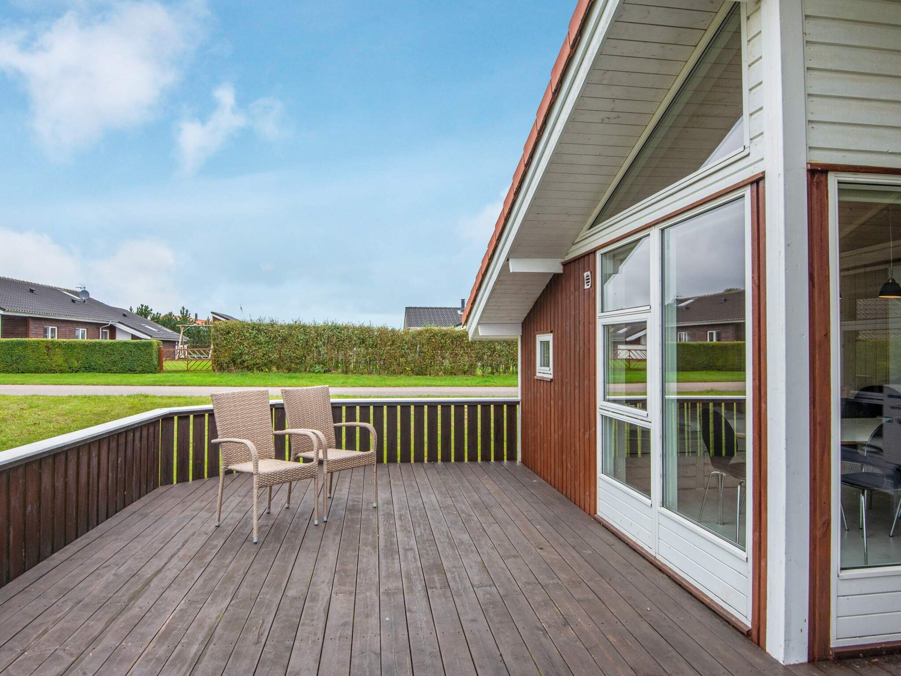 A wooden deck with outdoor furniture, a glass door leading to a covered area, and a view of a residential neighborhood.