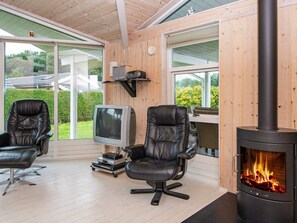 A cozy room with a fireplace, two leather chairs, a television, and a window overlooking a garden. - 4 Star Holiday Home in Juelsminde (Horsens)