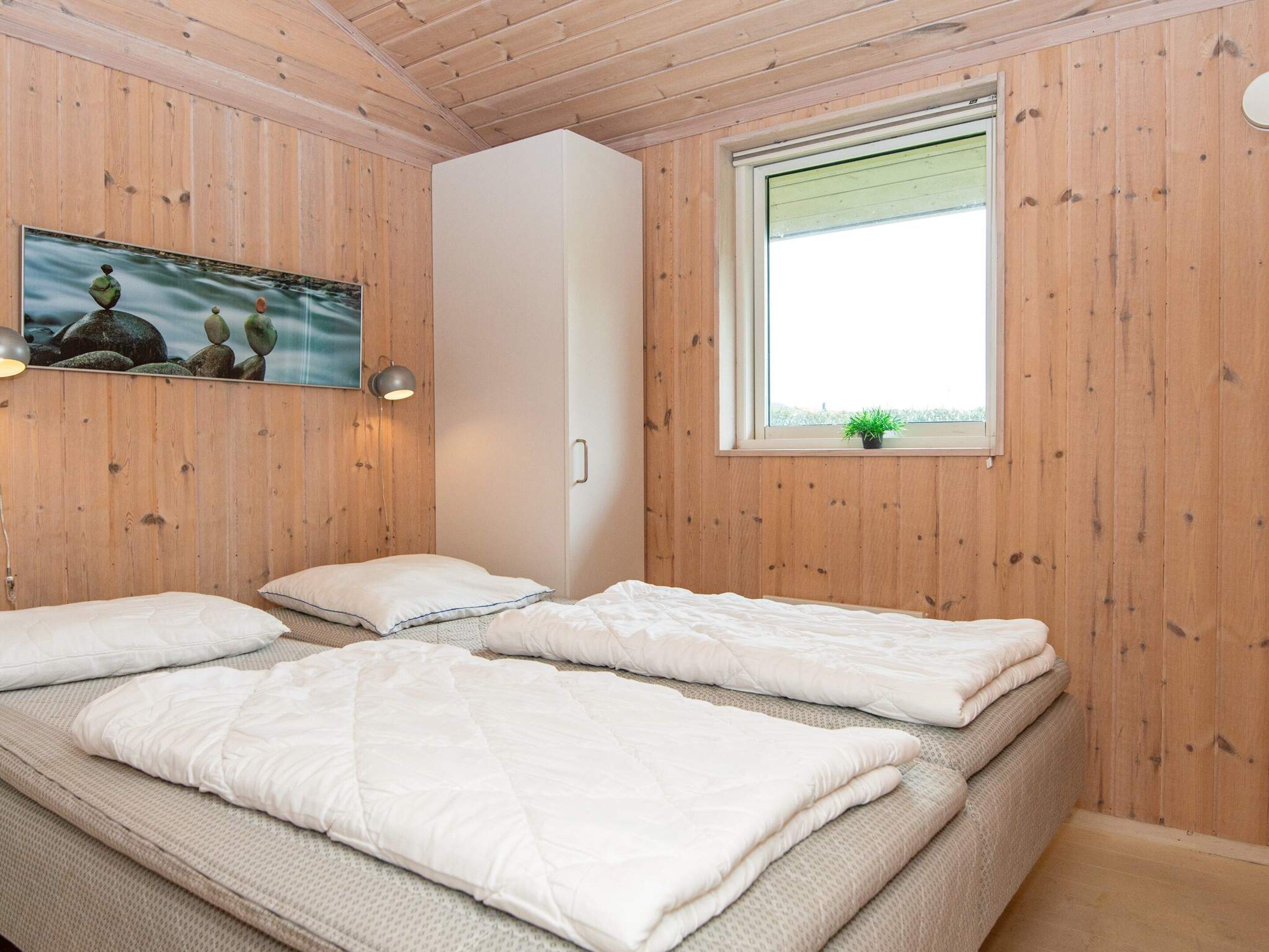 A room with wooden walls, a bed with white bedding, a window with a plant, and a painting on the wall.