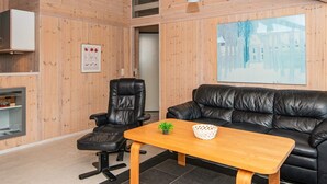Een modern interieur met een houten wand, een zwarte leren bank, een houten bijzettafeltje, een zwarte bureaustoel en een ingelijste foto.