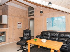 A modern interior with a wooden wall, a black leather sofa, a wooden coffee table, a black office chair, and a framed picture. - 4 Star Holiday Home in Juelsminde (Horsens)