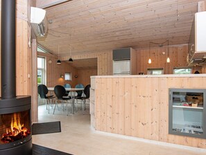 A wooden interior with a central fireplace, dining area, and kitchen. - 4 Star Holiday Home in Juelsminde (Horsens)