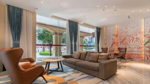A modern hotel lobby with a sofa, chairs, a round table, and large windows offering a view of the outdoors. - Yuemei Wanxiang Hotel (Zunyi)