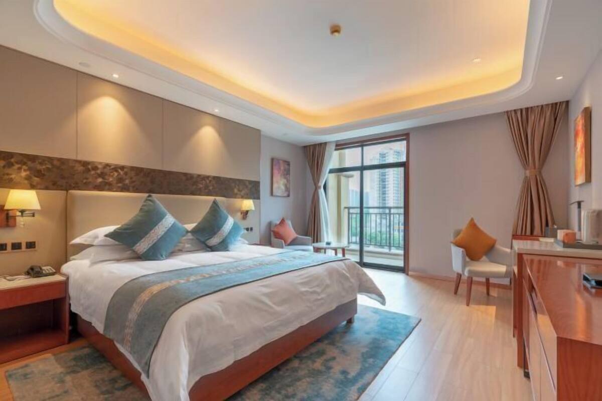 A modern hotel room with a large bed, bedside tables, a desk, and a view of the city.