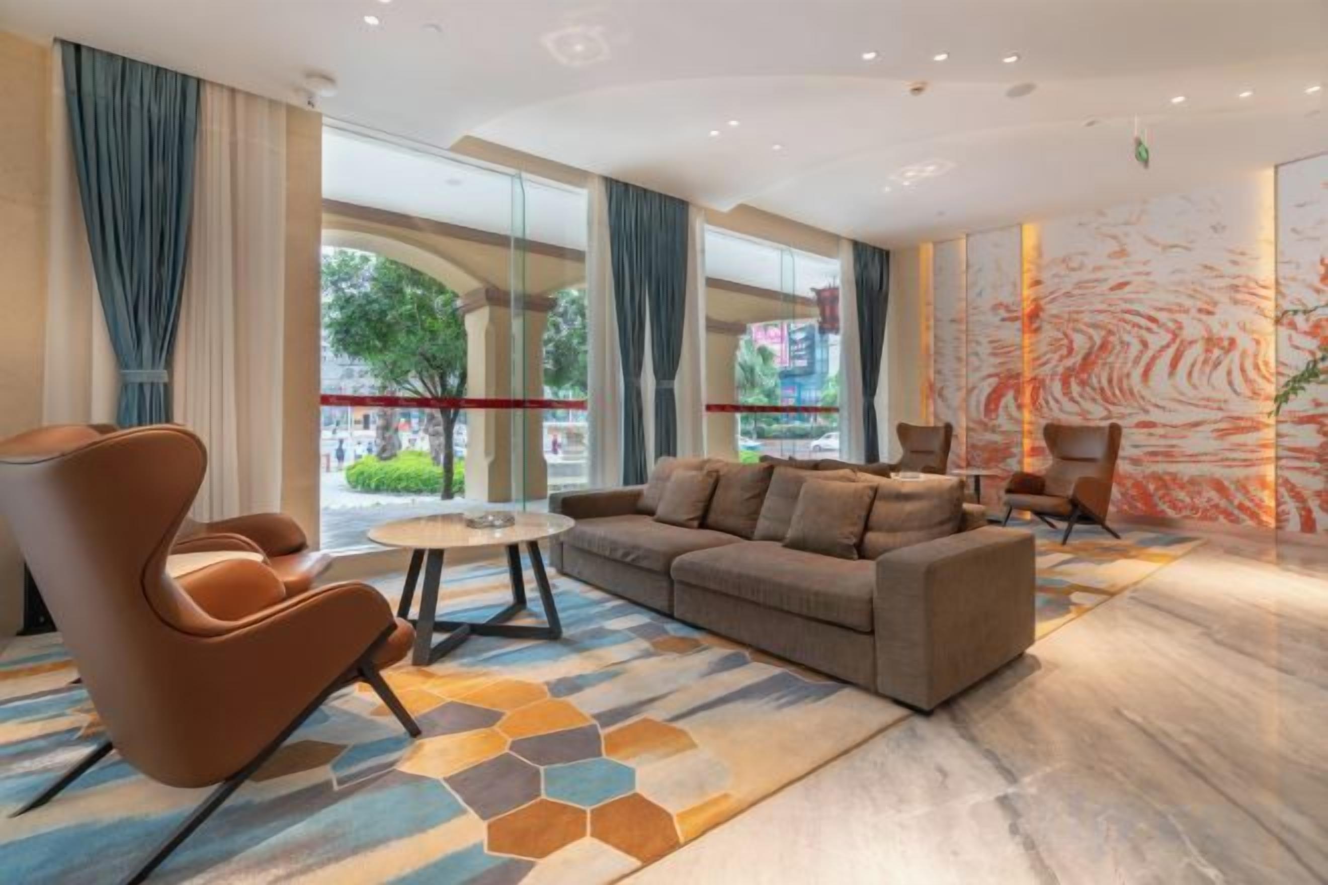 Un hall d’hôtel moderne, doté d’un canapé, de fauteuils, d’une table basse et de grandes fenêtres donnant sur l’extérieur.