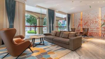 Un moderno vestíbulo de hotel con un sofá, sillones, una mesa de centro y ventanas amplias que ofrecen vistas al exterior.