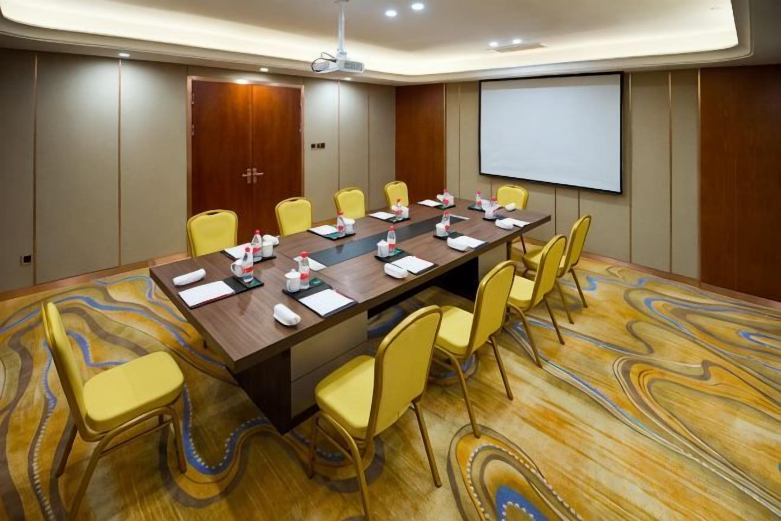 A conference room with a long table, yellow chairs, and a projector screen.