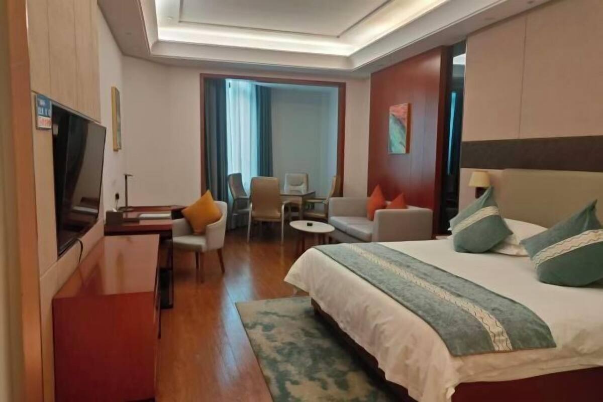 A hotel room with a bed, a desk, a chair, a small table, and a TV.