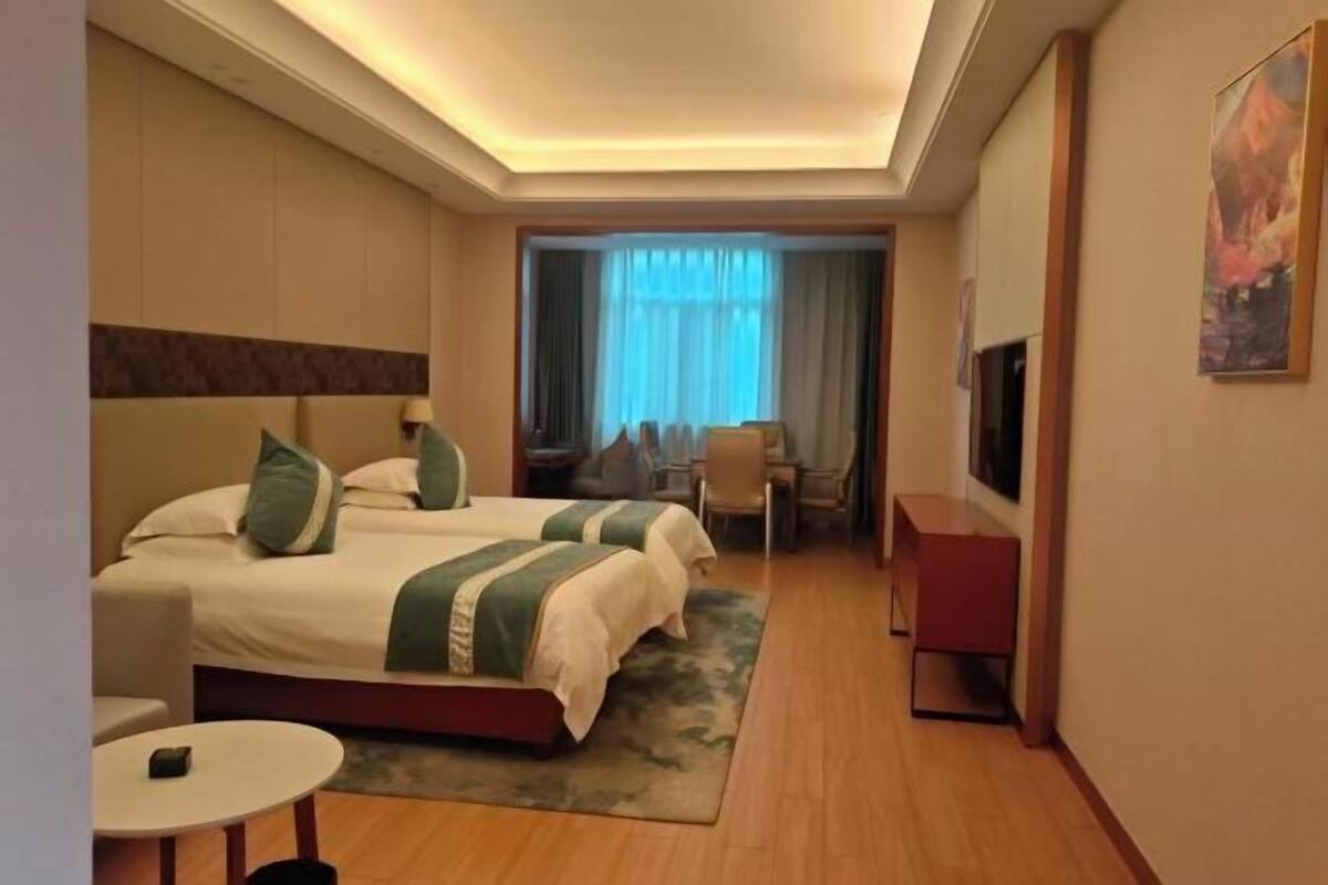 A hotel room with two beds, a desk, a chair, a TV, and a small table.