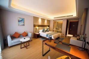 Una habitación de hotel moderna con una cama, un sofá y una pequeña mesa. Hay un cuadro en la pared y una puerta que da a otra habitación.