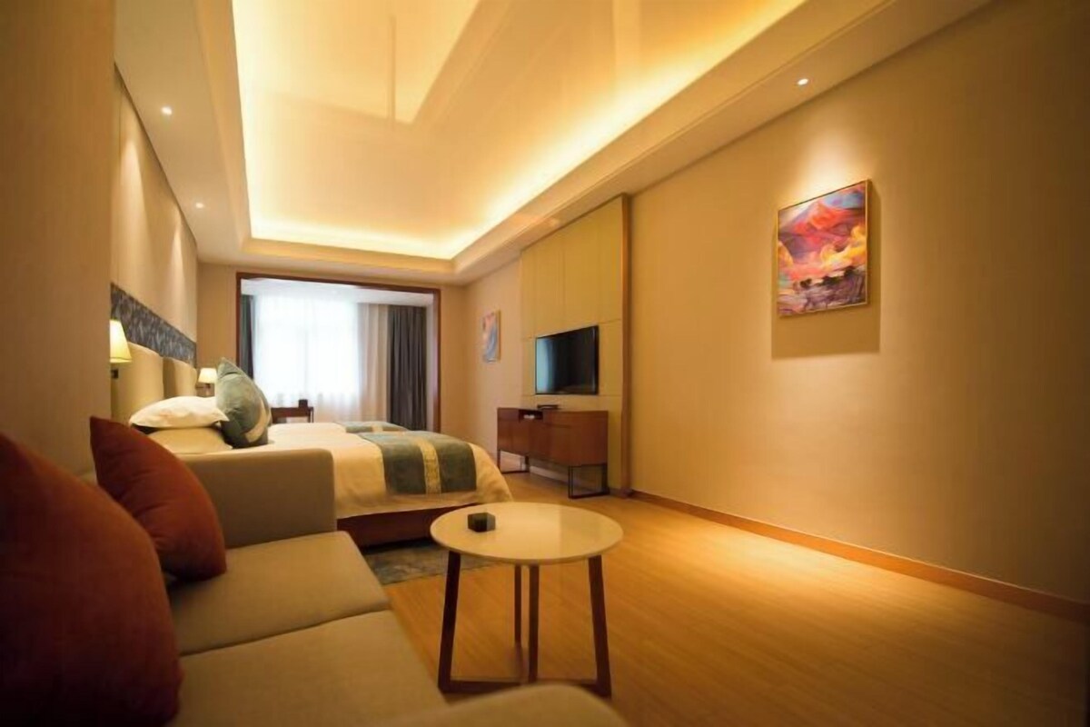 A hotel room with a bed, a sofa, a TV, a small table, and a painting on the wall.