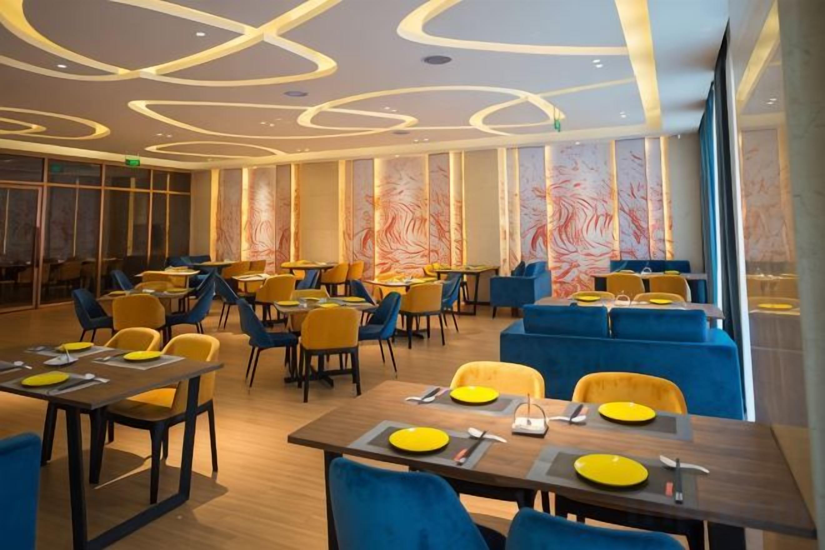 A restaurant with multiple tables and chairs, featuring a modern ceiling design and large windows.