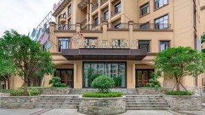 A hotel entrance with a stone staircase leading up to the door, surrounded by greenery and a stone planter. - Yuemei Wanxiang Hotel (Zunyi)