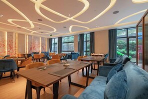 A modern dining area with tables and chairs, large windows, and a blue sofa. - Yuemei Wanxiang Hotel (Zunyi)